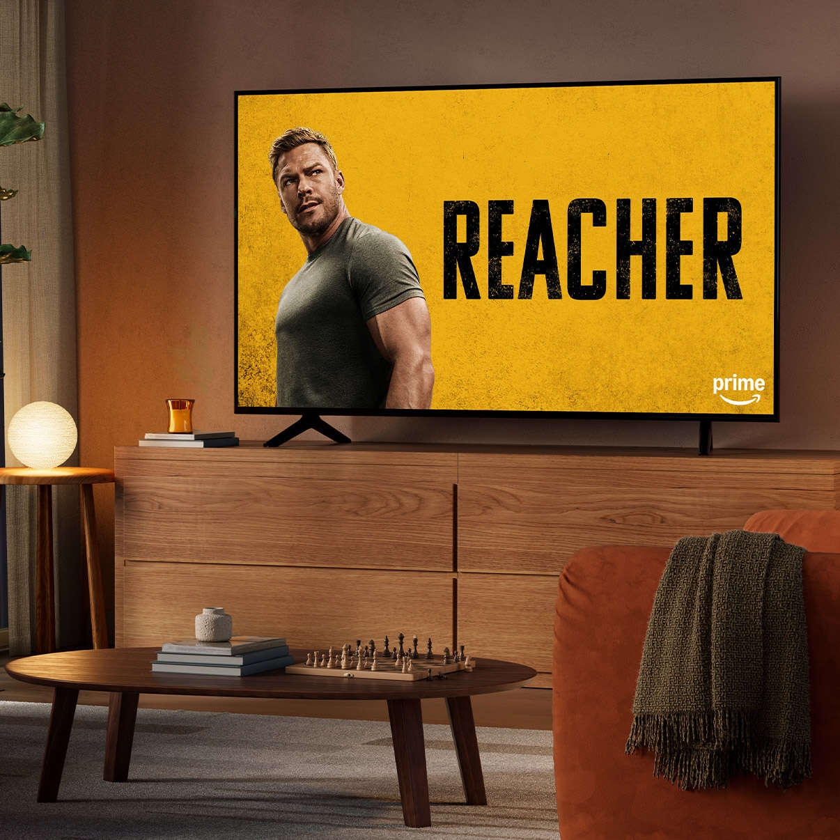 A dimly lit living room at night with the TV on an entertainment console. Reacher is on screen. 
