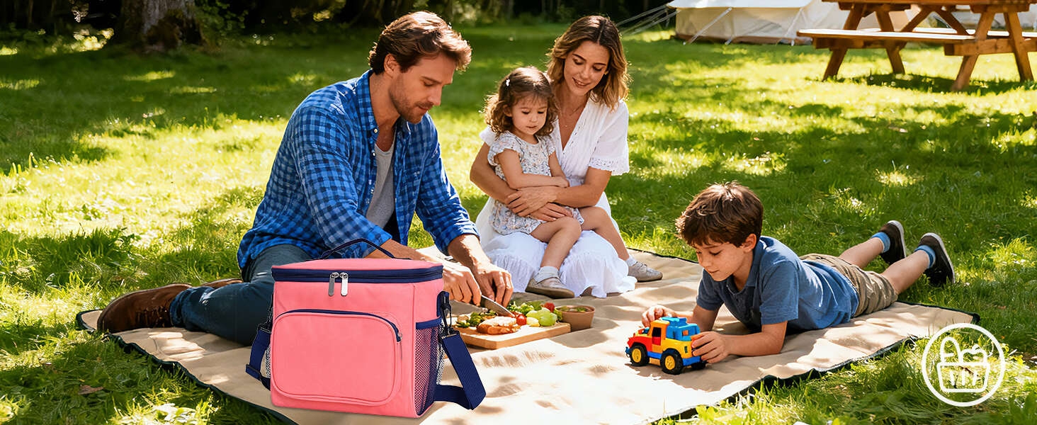Outdoor picnic setting with people relaxing on blankets in a grassy park area with trees and a picnic table visible in background.