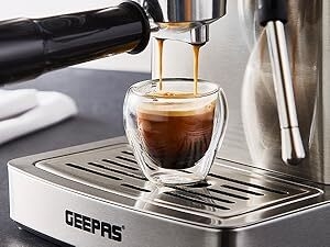 Espresso machine pouring coffee into a double-walled glass cup on a metal drip tray. Brand name 'GEEPAS' visible on the machine.