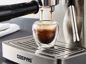 Espresso machine pouring coffee into a double-walled glass cup on a metal drip tray. Brand name 'GEEPAS' visible on the machine.