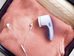 White earbuds and small purple-white digital thermometer displayed on pink knit fabric background