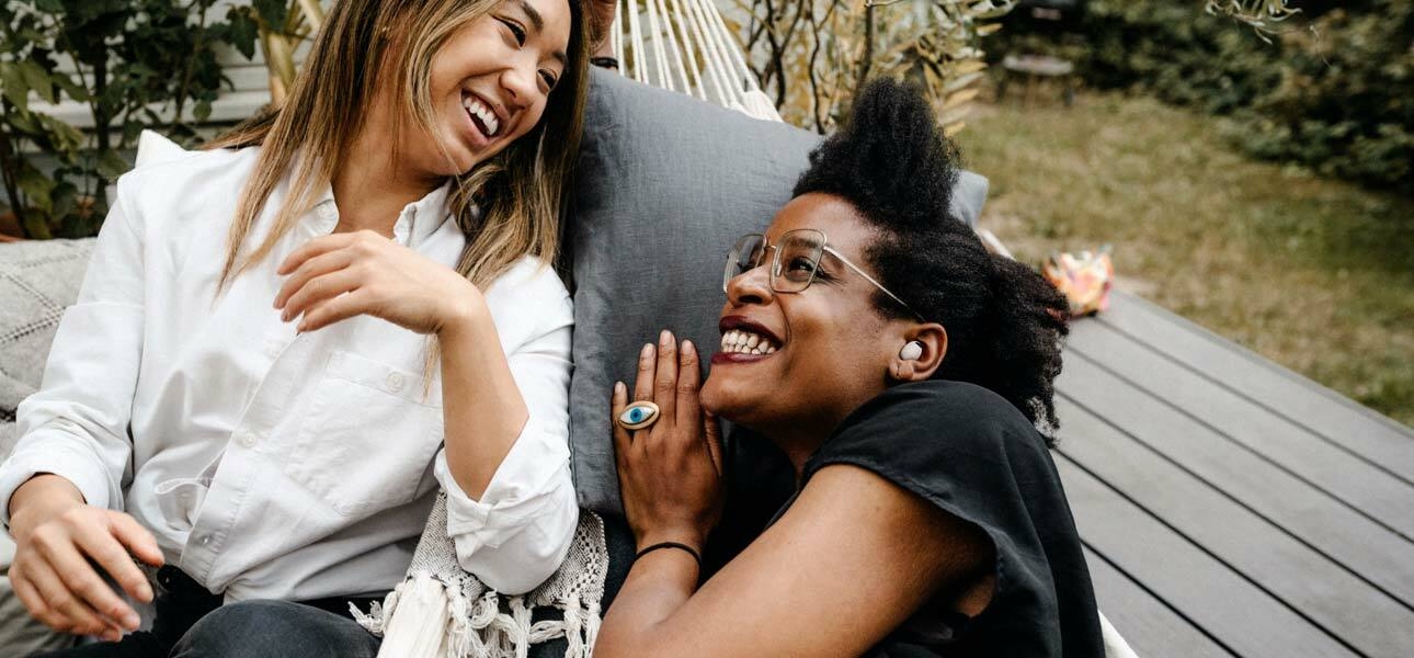 Two women laughing and having a conversation while facing each other. The woman on the right has …