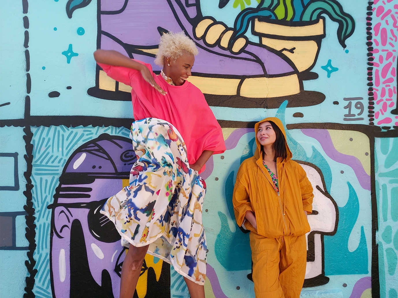 Photo captured by Galaxy A80âs Wide-angle lens of two women, one tall and one short, in front of a graffiti wall.