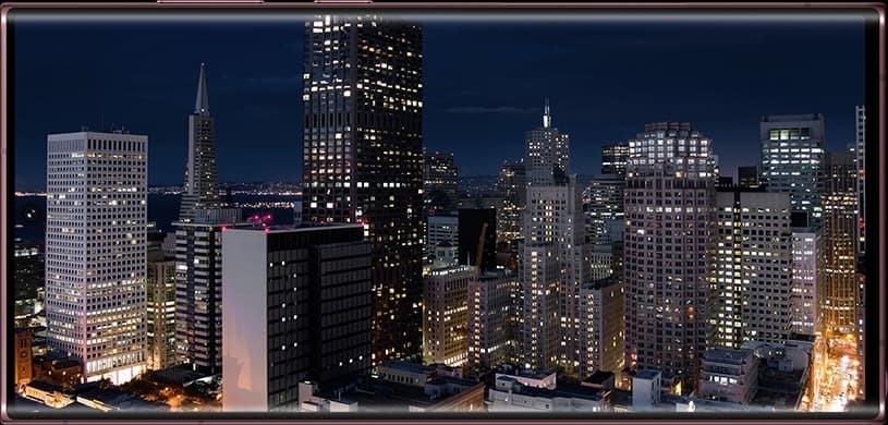 A view of an evening cityscape changes to become daytime. As the sky darkens to show a late night sky, it zooms out to become an image on Galaxy S22 Ultra's screen, the time lapse demonstrating how long the battery life lasts.