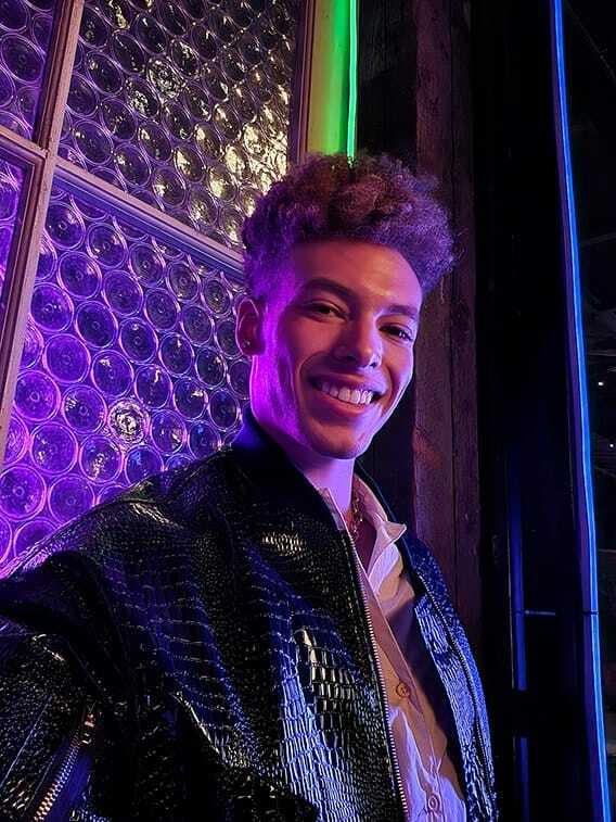 A man takes a selfie at a dark venue with colored lights. His face is bright and colors are …